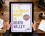 A framed poster with the text "IT IS SATURDAY NIGHT IN DEATH VALLEY LSU" and a tiger logo, held by a person's hands.