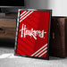 A framed poster with the word "Huskies" written on it, placed on a carpeted floor next to a wooden chest.