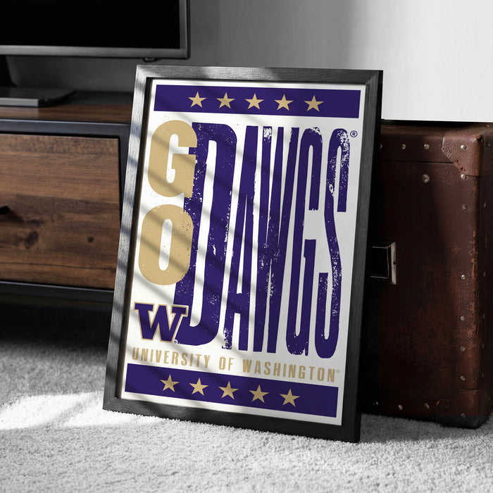 A framed poster with the text "GO DAWG'S" and "UNIVERSITY OF WASHINGTON" printed on it, placed on a carpeted floor next to a wooden chest.