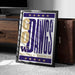 A framed poster with the text "GO DAWG'S" and "UNIVERSITY OF WASHINGTON" printed on it, placed on a carpeted floor next to a wooden chest.