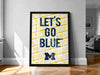 A framed poster with the text "LET'S GO BLUE" displayed prominently on it, which is a motivational message related to the Michigan State University (MSU) football team.