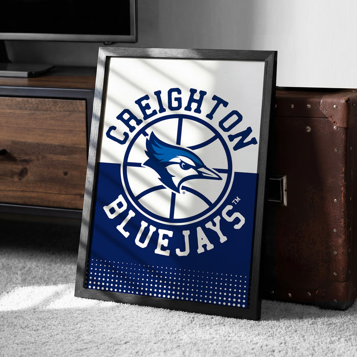 A framed poster of the Creighton Bluejays basketball team, featuring the team's logo and name, is displayed on a carpeted floor next to a wooden chest.