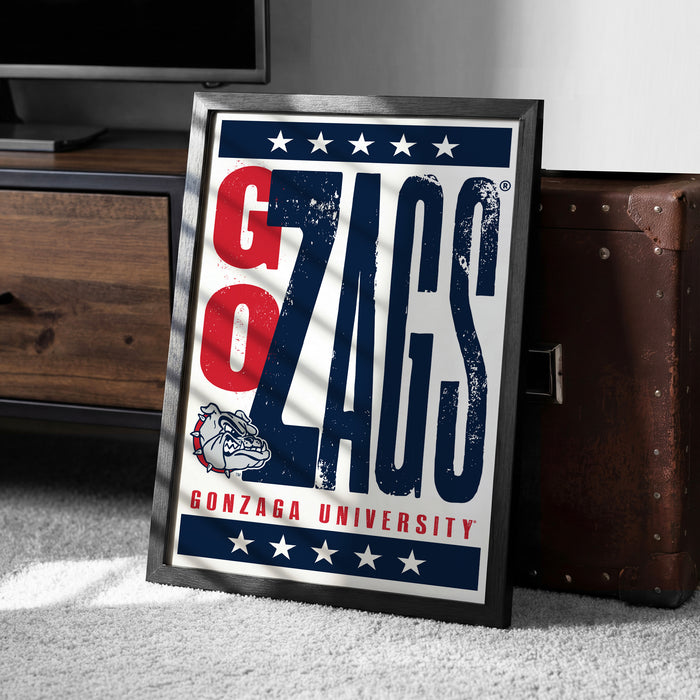 A framed poster with the text "GONZAGA UNIVERSITY" and a bulldog graphic, placed on a carpeted floor next to a wooden chest.