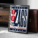 A framed poster with the text "GONZAGA UNIVERSITY" and a bulldog graphic, placed on a carpeted floor next to a wooden chest.