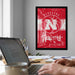 a framed poster of the Nebraska Huskers basketball team on the wall, with a person's hands typing on a laptop in the foreground.