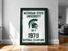 A framed poster on a wall celebrating the Michigan State University's 1979 National Champions, featuring the university's logo and the text "Michigan State University 1976-1979 NATIONAL CHAMPIONS".