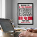 a framed poster with text on it, hanging on a wall next to a laptop.