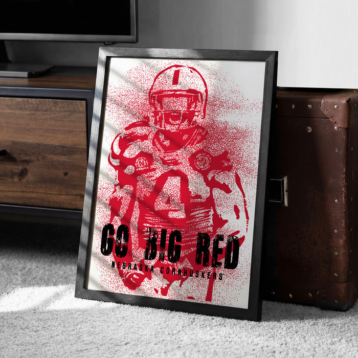 A framed poster featuring a red football player with the text "GO BIG RED" and "Nebraska Cornhuskers" printed on it.