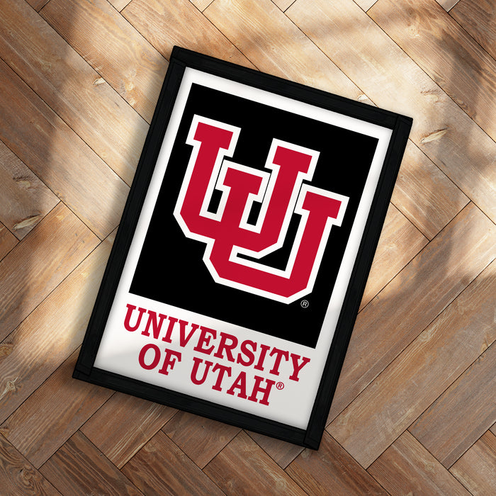 A framed poster with the University of Utah logo and text is displayed on a wooden floor.