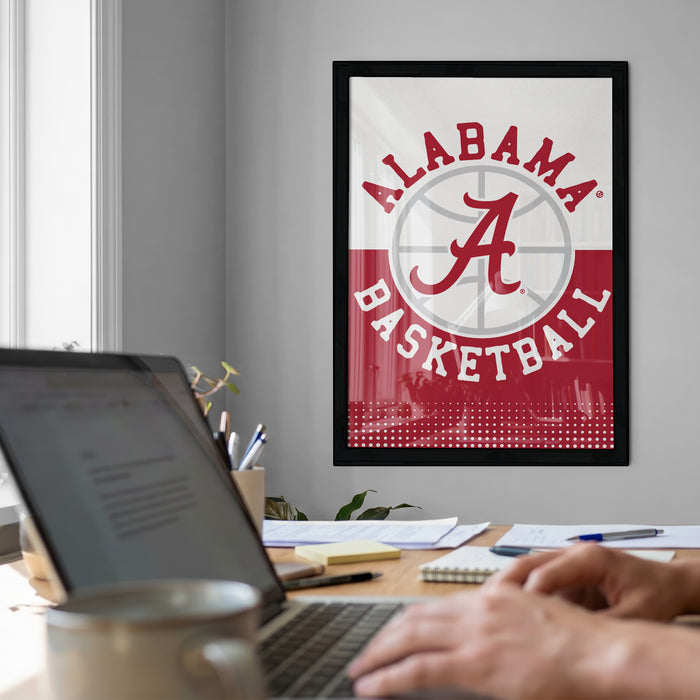 a framed poster of the Alabama basketball team on the wall, with a laptop and a coffee cup on a desk in the foreground.