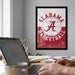 a framed poster of the Alabama basketball team on the wall, with a laptop and a coffee cup on a desk in the foreground.