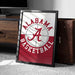 A framed poster with the Alabama basketball logo is displayed on a carpeted floor next to a wooden chest.