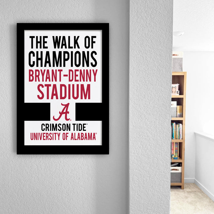a framed sign that reads "The walk of champions BRYANT-DENNY STADIUM A CRIMSON TIDE UNIVERSITY OF ALABAMA" on a wall.