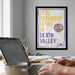 a framed poster with the text "IT IS SATURDAY NIGHT IN DEATH VALLEY" and a tiger logo, hanging on a wall above a desk with a laptop and other items.