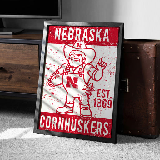 A framed poster of a Cornhuskers football team mascot, featuring the word "NEBRASKA" and the year "EST. 1869" on the poster.