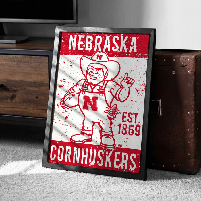 A framed poster of a Cornhuskers football team mascot, featuring the word "NEBRASKA" and the year "EST. 1869" on the poster.