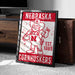 A framed poster of a Cornhuskers football team mascot, featuring the word "NEBRASKA" and the year "EST. 1869" on the poster.