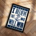 A framed poster with the text "I Believe That We Will Win" and an anchor symbol, placed on a wooden floor.