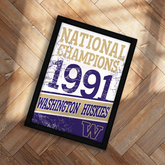 A framed poster with the text "NATIONAL CHAMPIONS 1991 WASHINGTON HUSKIES" printed on it, placed on a wooden floor.