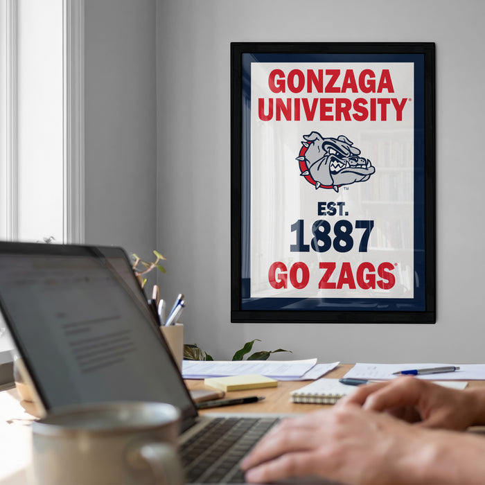 a framed poster of the University of Gonzaga, with a person's hands typing on a laptop in the foreground.