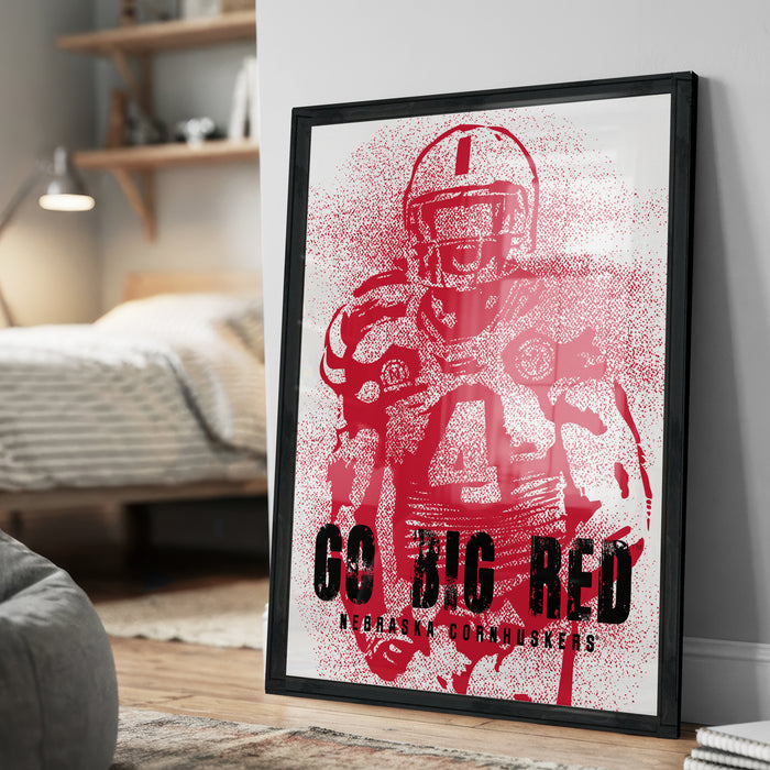 A framed poster featuring a red football player with the text "GO BIG RED" and "NEBRAK CORNHUSKERS" printed on it.