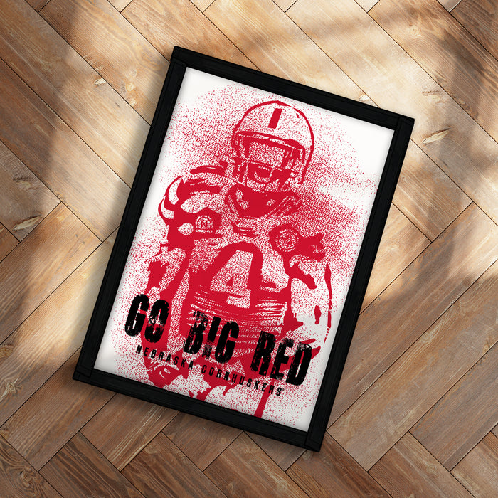 A framed poster with a red and white design featuring a football player, placed on a wooden floor.