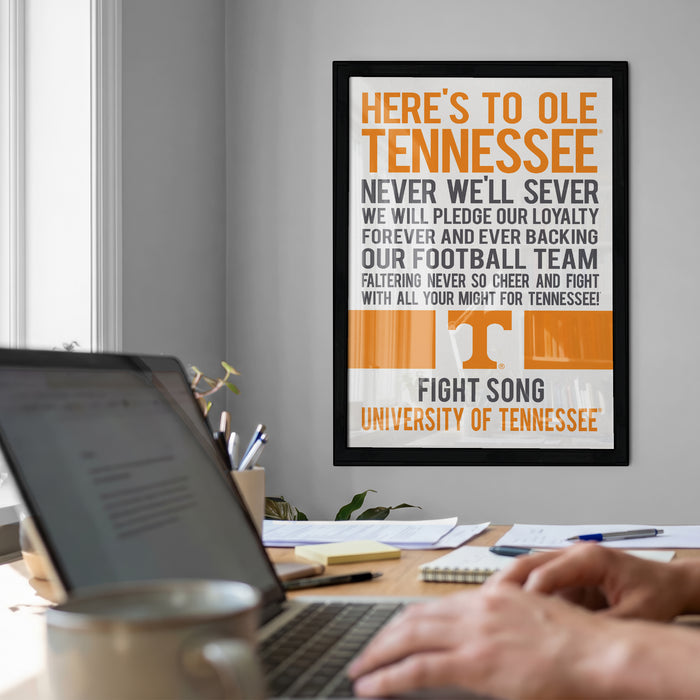 a framed poster with a message about the University of Tennessee, along with a laptop and some office supplies on a desk.