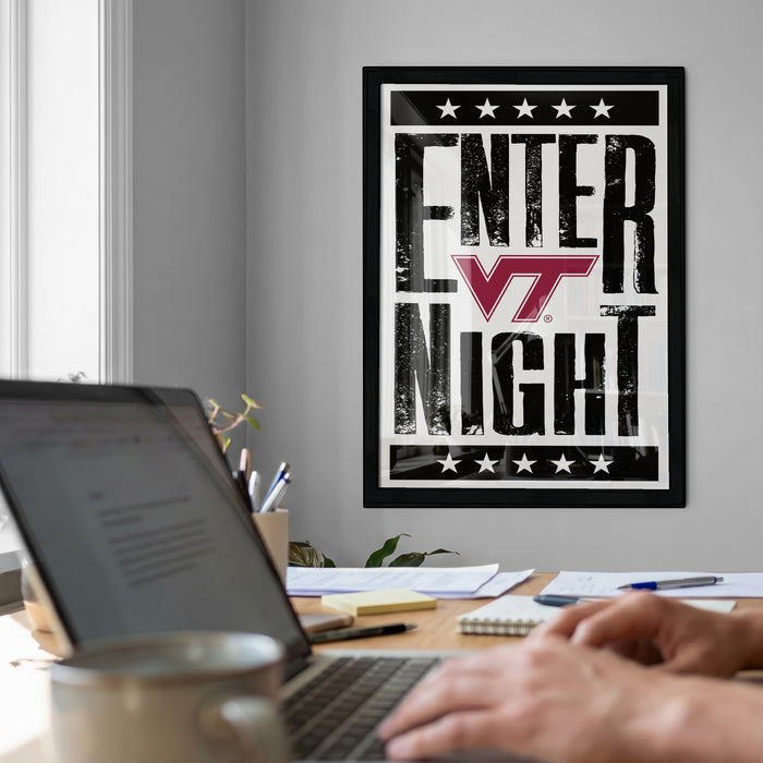a person working on a laptop at a desk, with a framed poster on the wall behind them that reads "ENTER NIGHT".