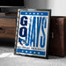 A framed poster with the text "GAYS" and a blue bird logo, placed on a carpeted floor next to a brown suitcase.