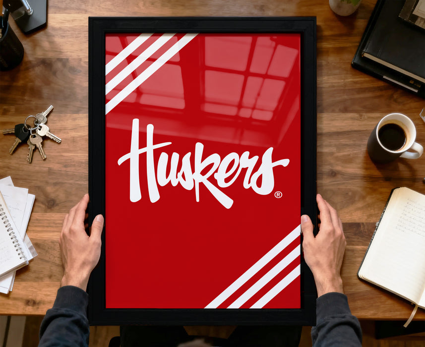 A person is holding a framed picture with the word "Huskies" written on it, which is displayed on a wooden desk.