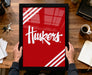 A person is holding a framed picture with the word "Huskies" written on it, which is displayed on a wooden desk.