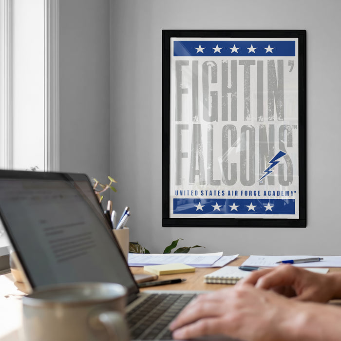 A framed poster with the text "FIGHTIN' FALCONS" hangs on a wall above a desk with a laptop and other office supplies.