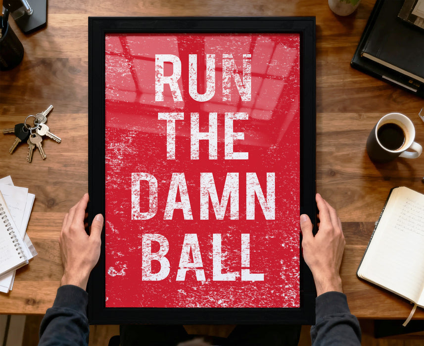 A person is holding up a framed poster with the text "RUN THE DAMN BALL" on it, which appears to be a motivational quote.