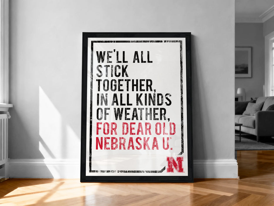 A framed poster with the text "WE'LL ALL STICK TOGETHER, IN ALL KINDS OF WEATHER, FOR DEAR OLD NEBRASKA U."