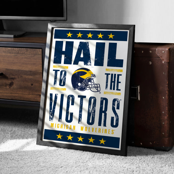A framed poster with the text "Hail to the Victors" and a football helmet graphic, along with the text "MICHIGAN WOLVERINES" at the bottom.