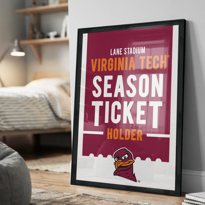 A framed poster advertising Virginia Tech's season ticket holder, with a bed and bookshelf visible in the background.