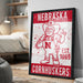 A framed poster of a cartoon character wearing a Nebraska hat and overalls, with the text "NEBRASKA CORNHUSKERS" printed on it.
