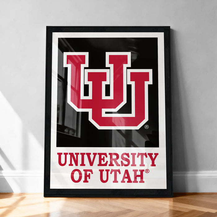 A framed poster of the University of Utah logo is displayed on a wooden floor against a white wall.