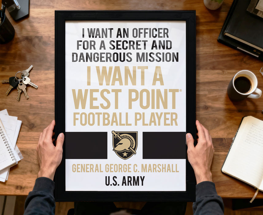 A person is holding up a framed sign with text that says "I want an officer for a secret and dangerous mission I want a West Point Football Player General George C. Marshall U.S. Army".