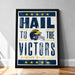 A framed poster with the text "Hail to the Victors" and a football helmet graphic, promoting Michigan Wolverines.