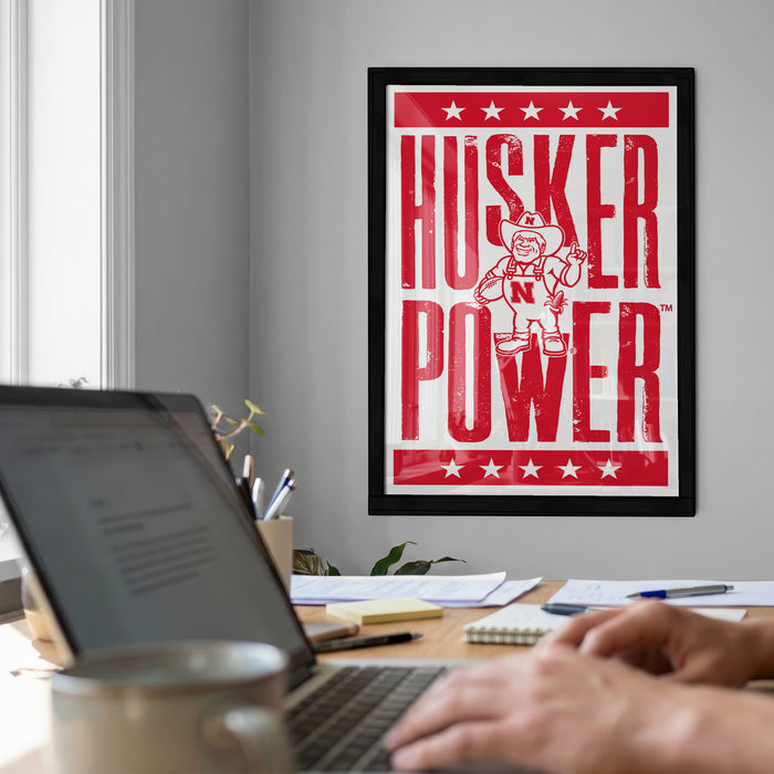 a person working on a laptop computer, with a framed poster of a character on the wall behind them.