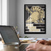 a person working on a laptop at a desk, with a framed poster of a military symbol hanging on the wall behind them.