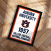 A framed poster with the text "Auburn University 1957 College Football National Champions" on it, placed on a wooden floor.