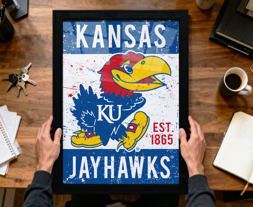 A framed poster of the Kansas University Jayhawks, a sports team, is being held by a person's hands.