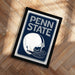 A framed poster of a football helmet with the text "PENN STATE" on it, placed on a wooden floor.