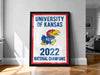 A framed poster on a wall celebrating the University of Kansas' national championship in the year 2023.