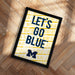 A framed poster with the text "LET'S GO BLUE" printed on it, placed on a wooden floor.