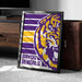 A framed poster of the LSU (Louisiana State University) logo is displayed on a carpeted floor next to a wooden chest.