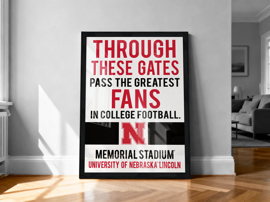 A framed sign on a wall that reads "THROUGH THESE GATES PASS THE GREATEST FANS IN COLLEGE FOOTBALL. N" and "MEMORIAL STADIUM UNIVERSITY OF NEBRASKA LINCOLN".