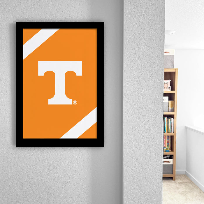 a framed poster of the letter "T" on an orange background, hanging on a wall.